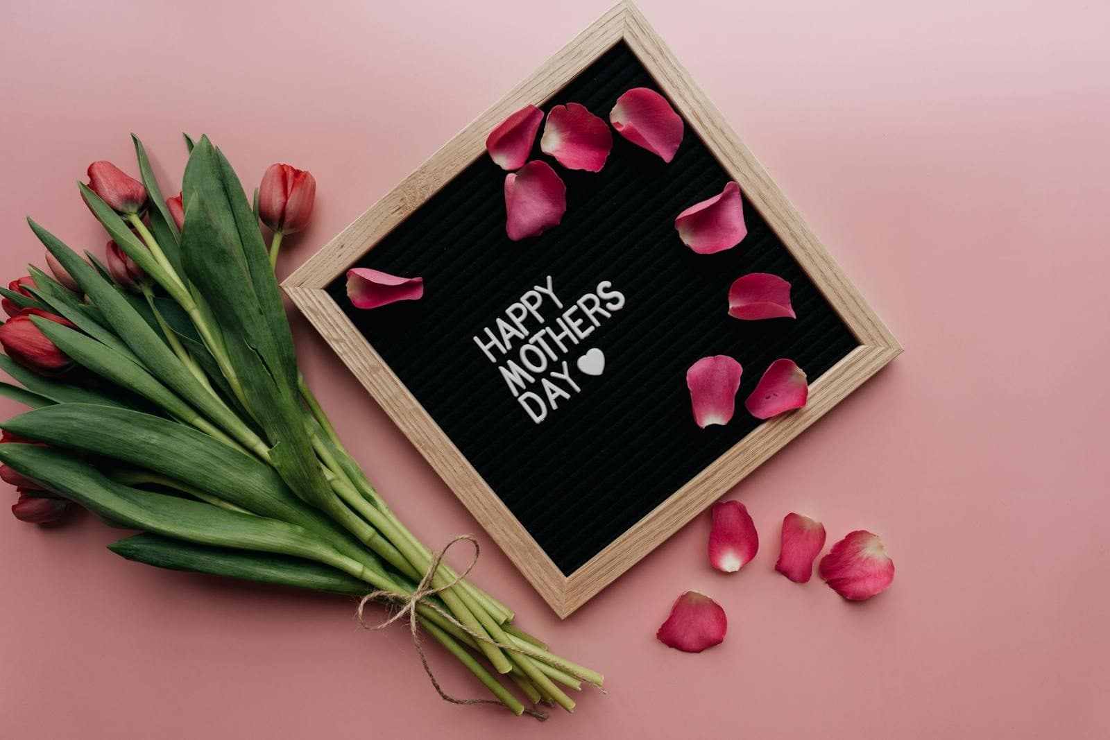Beautiful Mother's Day arrangement with tulips and letterboard on pink background.